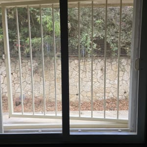 חלון עם סורגים ונוף של גדר וצמחייה בחוץ