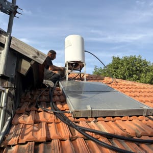 אדם מתקין דוד שמש על גג רעפים עם צינורות מחוברים