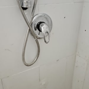 ברז מקלחת עם צינור מתכת על קיר לבן