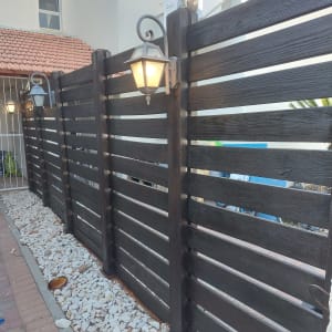 גדר עץ צבועה בצבע כהה עם מנורות תלייה