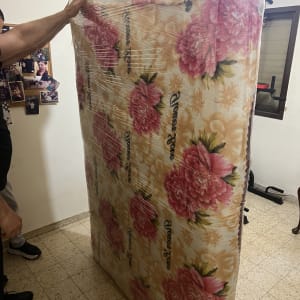 אדם מחזיק מזרן עטוף בניילון בחדר