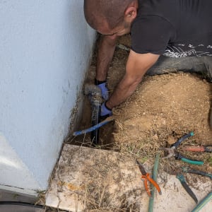 אדם עובד על תיקון צנרת ליד קיר חיצוני