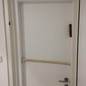 דלת לבנה עם ידית מתכת ומוט עץ לרוחב