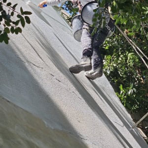 אדם עם קסדה צובע קיר חיצוני בעזרת רולר.