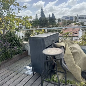 מרפסת עם צמחייה, כיסא מתכת וארון עץ.