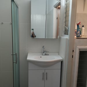 חדר אמבטיה עם כיור, מראה וחומרי ניקוי על המדף