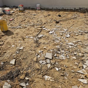 שברי אריחים וכלי עבודה על רצפת חול באתר שיפוץ