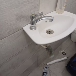 כיור עם ברז, צינור גמיש וכלי עבודה על הרצפה