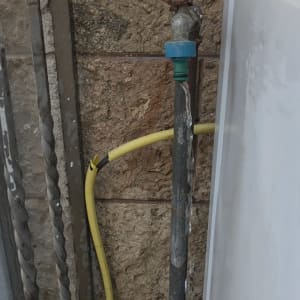 ברז מים עם צינור צהוב על קיר אבן