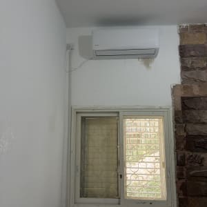 מזגן מותקן על קיר ליד חלון עם סורגים