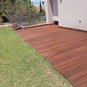 דק עץ חום ליד דשא ירוק בגינה