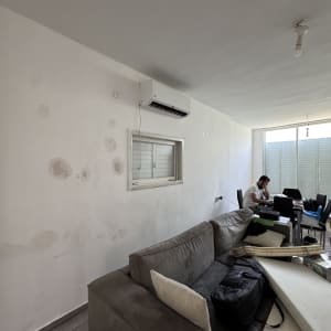 קיר עם סימני תיקון וצבע, ספה ואדם יושב ליד שולחן