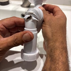 ידיים מחזיקות צינור שבור בכיור