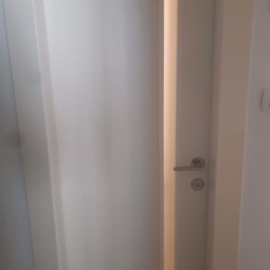 דלת פנים לבנה מעוצבת עם פס זכוכית אנכי וידית כסופה