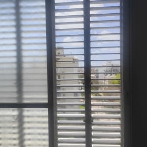 תריסים לבנים על חלון עם נוף עירוני ברקע