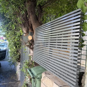 גדר אלומיניום ליד עץ ברחוב עם פח ירוק