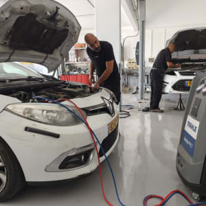 שני מכונאים עובדים על רכבים עם מכשיר חשמלי וכבלים.