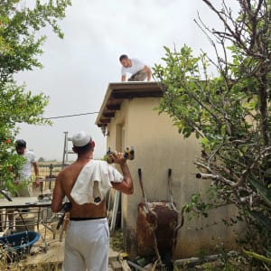 אדם מחזיק מקדחה ליד גג עם צמחייה מסביב