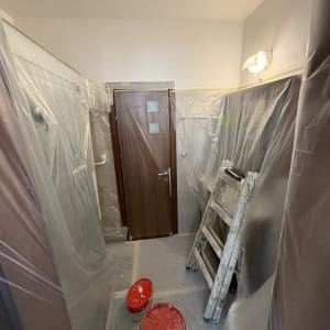 סולם ודליים בחדר מוכן לצביעה עם כיסויים פלסטיים.