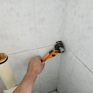 יד מחזיקה מפתח צינורות על קיר אריחים