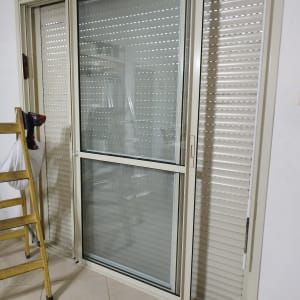 תריסים לבנים על חלון זכוכית עם מסגרת מתכת