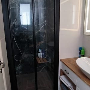 מקלחון זכוכית עם קירות שיש כהים וארון עץ עם כיור לבן