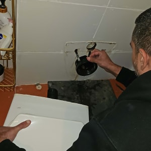 אדם מתקן צנרת עם כלים ליד קיר