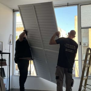 שני אנשים מרימים תריס אלומיניום גדול ליד חלון