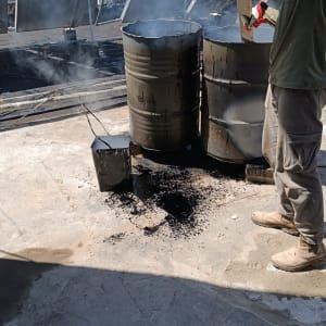 אדם עם כפפות ליד חביות זפת מעשנות