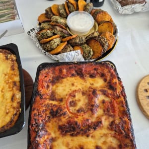 מגוון מאכלים על שולחן, כולל לזניה, ירקות מטוגנים ובקבוקי יין.