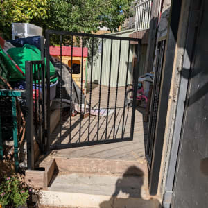 שער מתכת פתוח עם צל של אדם על המדרכה