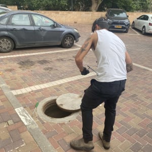 אדם ליד פתח ביוב בחניון עם מכוניות