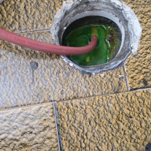 צינור אדום בתוך פתח ביוב עם נוזל ירוק