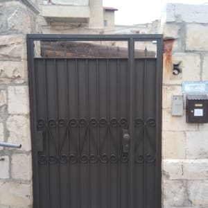 שער מתכת שחור עם עיטורים על קיר אבן