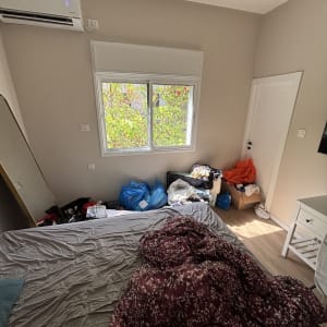 חדר שינה עם מיטה מבולגנת ושקיות בגדים על הרצפה