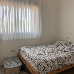 וילון לבן תלוי על חלון בחדר שינה עם מיטה מעץ