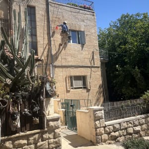 אדם עובד על קיר בניין בגובה עם ציוד בטיחות