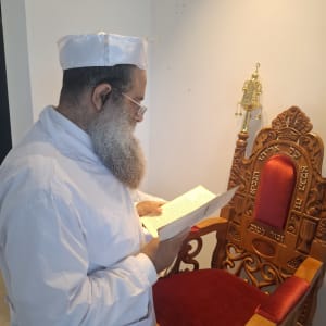 אדם בלבוש מסורתי קורא ספר ליד כיסא מעוטר