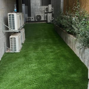 דשא סינתטי לצד שיחים ירוקים בגינה קטנה