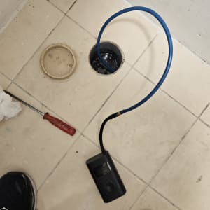 כלי עבודה וצינור כחול ליד פתח ניקוז ברצפה