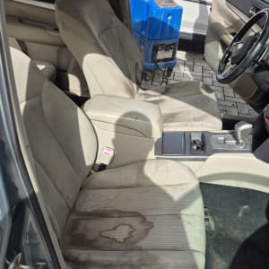 מושב רכב מלוכלך עם כתמים וכלי ניקוי כחול ברקע