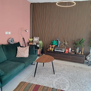 סלון מעוצב ומסודר עם ספה ירוקה, חיפוי עץ דקורטיבי ושולחן קפה