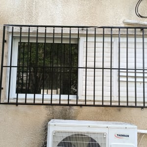 סורג מתכת על חלון עם תריסים לבנים