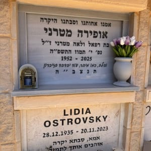 מצבה עם כיתוב בעברית ואנגלית, פרחים ונר זיכרון