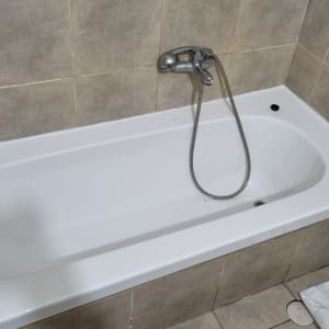 אמבטיה לבנה עם ברז מתכת וקירות מרוצפים