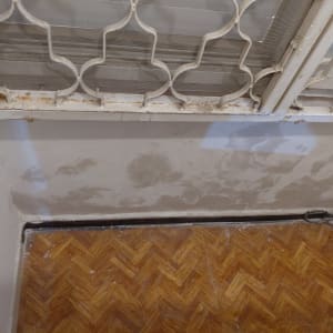 קיר עם סימני תיקון וצביעה ליד חלון עם סורגים.