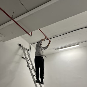 אדם על סולם מתקן צינור תקרה אדום