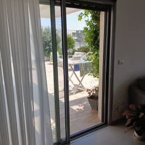 דלת הזזה מאלומיניום עם וילון לבן וצמחייה בחוץ