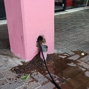 צינור שחור יוצא מקיר ורוד עם מים על הרצפה