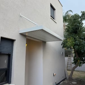 פרגולה אלומיניום מותקנת על קיר חיצוני של בית